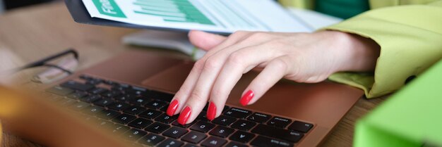 La mano della donna d'affari e la tenuta dei grafici finanziari tocca il laptop mentre si lavora in ufficio