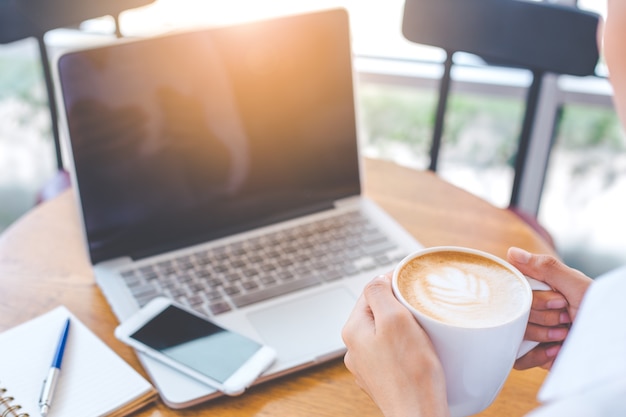 La mano della donna d&#39;affari tiene una tazza di arte ccoffee e funziona su un computer portatile.