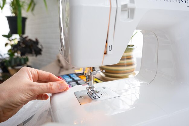 La mano della donna da vicino cuce il tulle sulla macchina da cucire elettrica Riempiendo il filo nell'ago da cucito regolando la tensione Comfort in casa layout hobby di una casalinga di strumenti per cucire