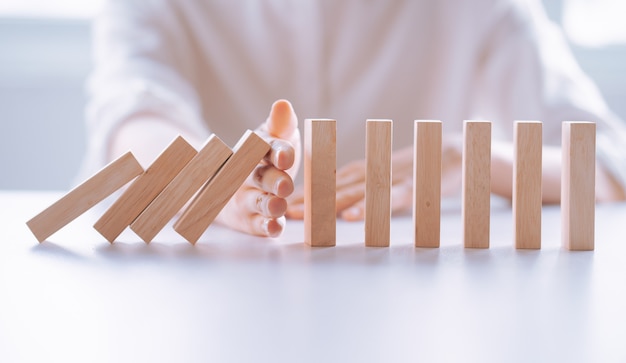 La mano della donna ferma l'effetto di crisi aziendale di domino in legno, concetto di protezione dai rischi