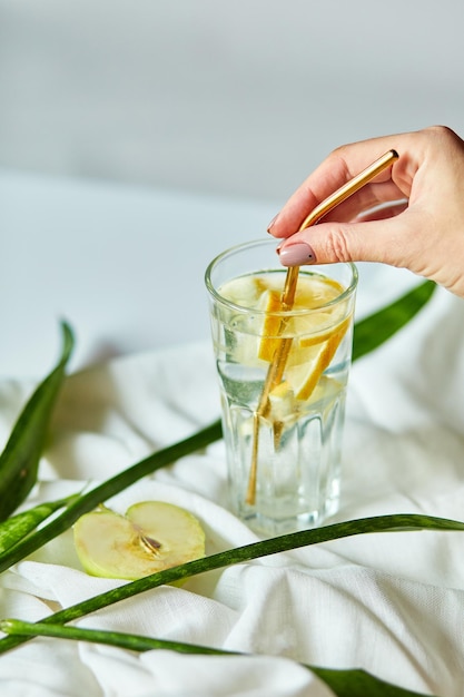 La mano della donna ha messo il tubo da cocktail ecologico in metallo in un bicchiere con acqua infusa di limone fresco fresco