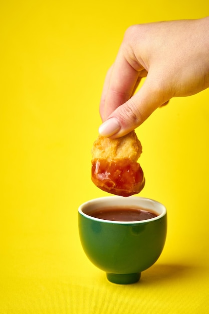 La mano della donna immerge le pepite di pollo in salsa rossa su sfondo giallo