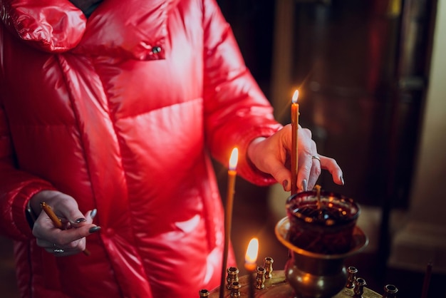 La mano della donna in una giacca rossa mette una candela della chiesa