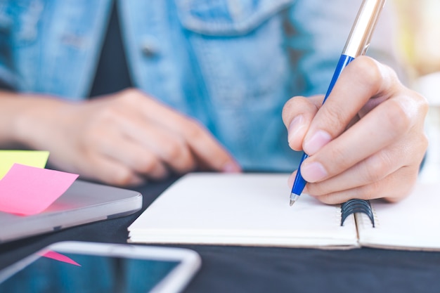 La mano della donna lavora in un computer portatile e sta scrivendo sul blocco note