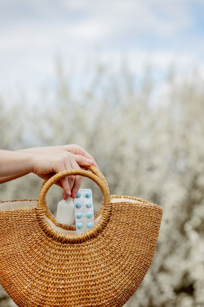 La mano della donna mette le pillole di allergia in borsa su fondo di fioritura