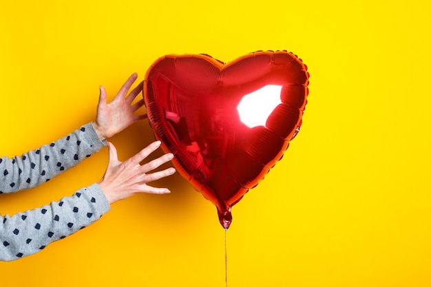 La mano della donna raggiunge la mongolfiera a forma di cuore su uno sfondo giallo.