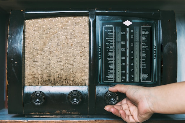 La mano della donna regola il pulsante del ricevitore radio vintage per ascoltare musica o notizie