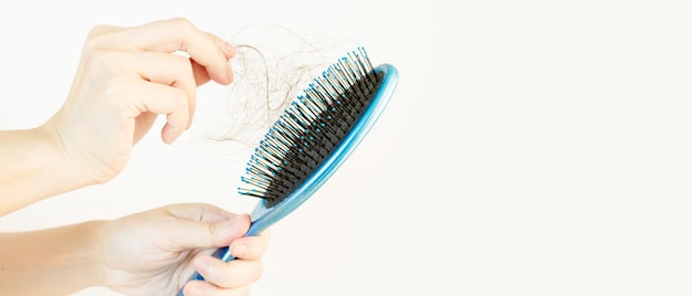 La mano della donna sta raccogliendo i capelli dalla spazzola blu su sfondo bianco.