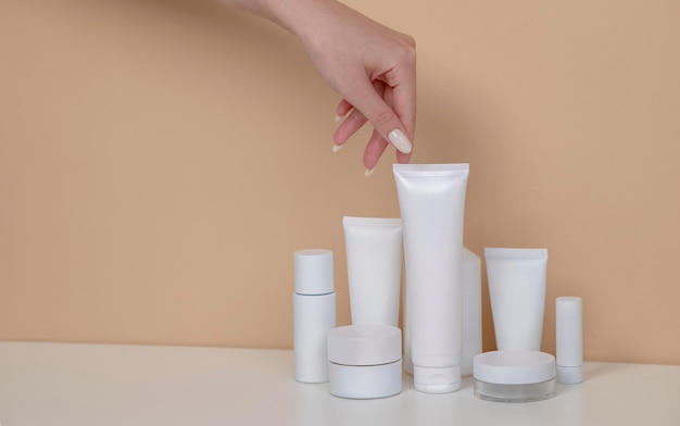 La mano della donna sta raccogliendo il flacone spray per tubo bianco mockup di imballaggio cosmetico vuoto su sfondo beige