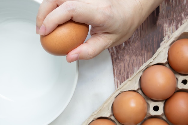 La mano della donna sta rompendo l'uovo fresco nella ciotola per prepararsi per cucinare