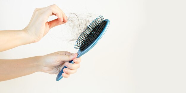 La mano della donna sta selezionando la caduta dei capelli dalla spazzola blu su sfondo bianco.