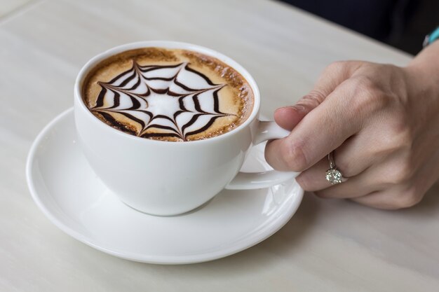 La mano della donna sta tenendo una tazza di caffè caldo.