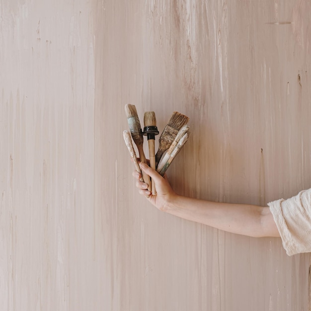 La mano della donna tiene i pennelli su sfondo beige neutro Concetto di arte minimalista