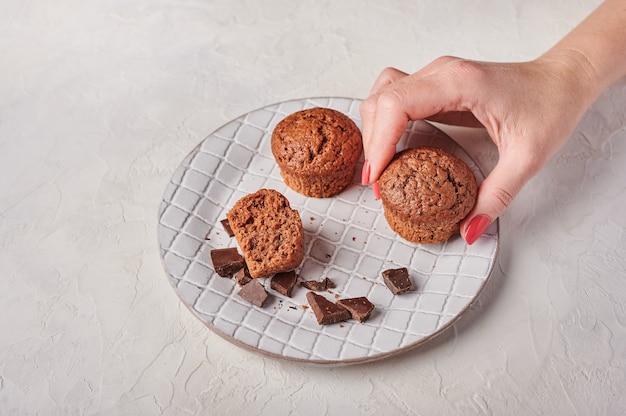 La mano della donna tiene un altro cupcake e pezzi di cioccolato nel piatto strutturato sulla luce di legno