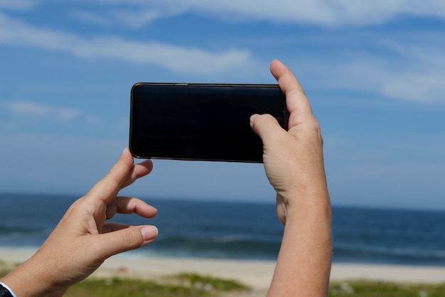 La mano della donna tiene un telefono cellulare per scattare foto della spiaggia