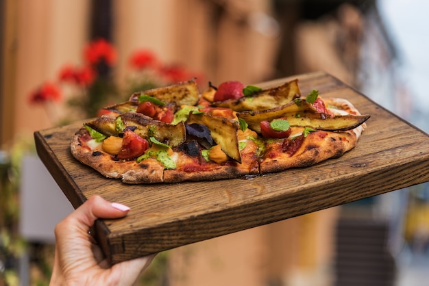 La mano della donna tiene un vassoio di legno con pinsa hummus e melanzane glassate