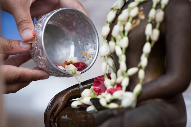 La mano della donna tiene una piccola ciotola per il bagno La statua del Buddha per la cerimonia di benedizione celebra Songkran