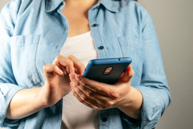 La mano della donna utilizza lo smartphone sul fondo grigio della parete