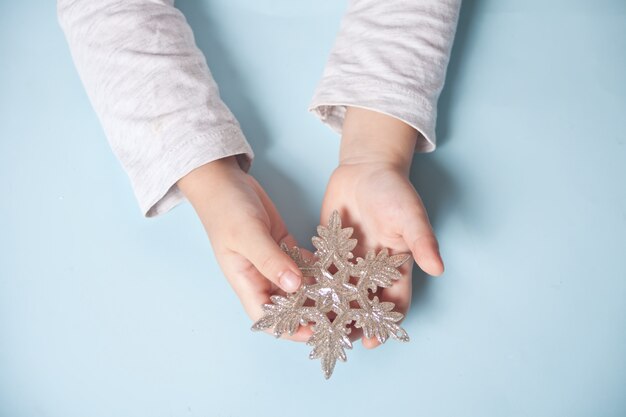 La mano della ragazza che tiene un grande fiocco di neve della decorazione di Natale in mani sull'azzurro