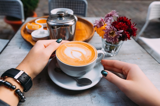 La mano della ragazza con un orologio e un braccialetto intorno a una tazza di caffè