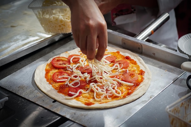 La mano dello chef ha messo il formaggio sulla pizza cruda in cucina.