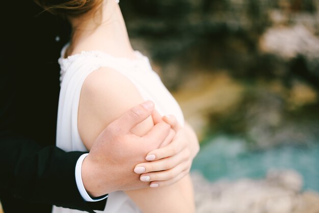 La mano dello sposo abbraccia la spalla della sposa in un vestito bianco primo piano