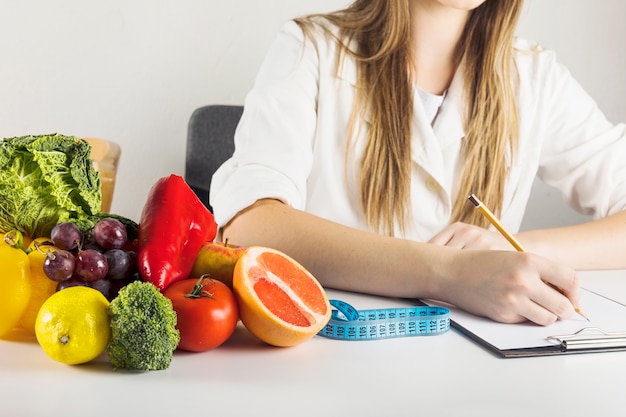 La mano di dietista scrivendo su Appunti con cibo sano sulla scrivania