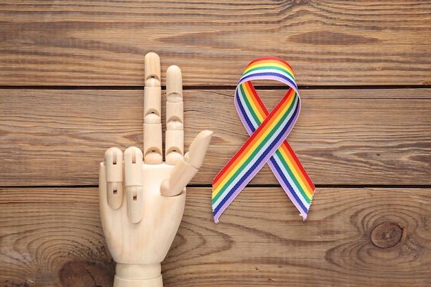 La mano di legno mostra il gesto di pace e il simbolo del nastro dell'orgoglio del nastro arcobaleno LGBT su sfondo di legno