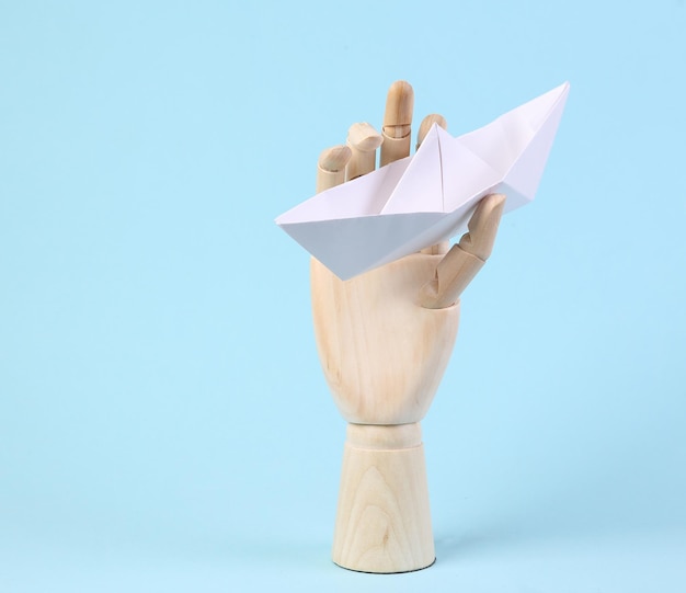 La mano di legno tiene la barca di carta origami su sfondo blu