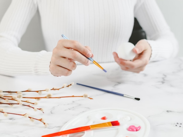 La mano di un'adolescente caucasica in un dolcevita bianco con un pennello e la seconda tiene un uovo