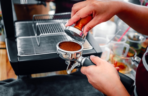 La mano di un barista che tiene un portafilter e un tamper del caffè che fa un caffè espresso