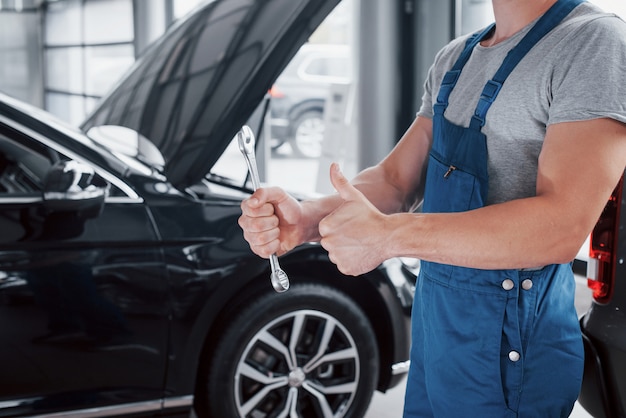 La mano di un meccanico con una chiave inglese in una zona combinata vicino all'auto nell'officina.