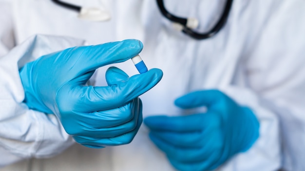 La mano di un medico o di un farmacista in guanti blu tiene una capsula con la medicina