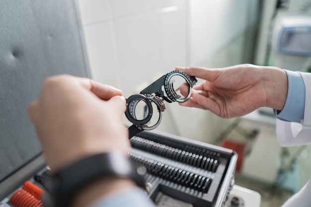 La mano di un medico tiene la montatura della lente sperimentale in una stanza di una clinica oculistica con lo sfondo della scatola del telaio degli occhiali