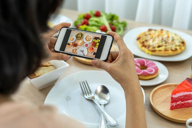 La mano di un recensore che usa un telefono cellulare per scattare foto del cibo al tavolo di un ristorante Scatta una foto per scrivere una recensione del ristorante da condividere su Internet