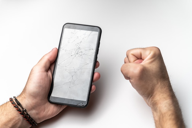 La mano di un uomo e un pugno chiuso con un telefono cellulare con uno schermo rotto.