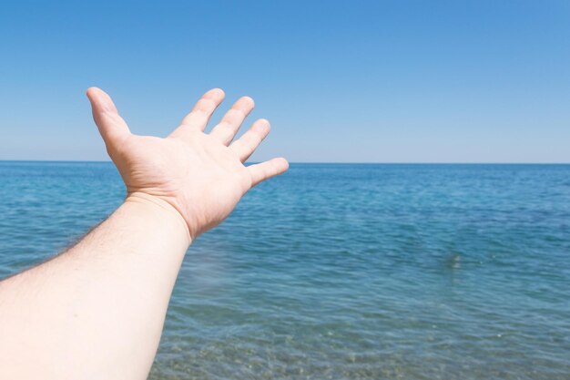 La mano di un uomo teso al mare in riva all'oceano Il concetto di libertà di viaggio ricreativo