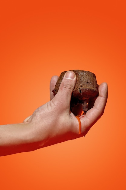 La mano di un uomo tiene un fondente al cioccolato da cui scorre il cioccolato su uno sfondo arancione