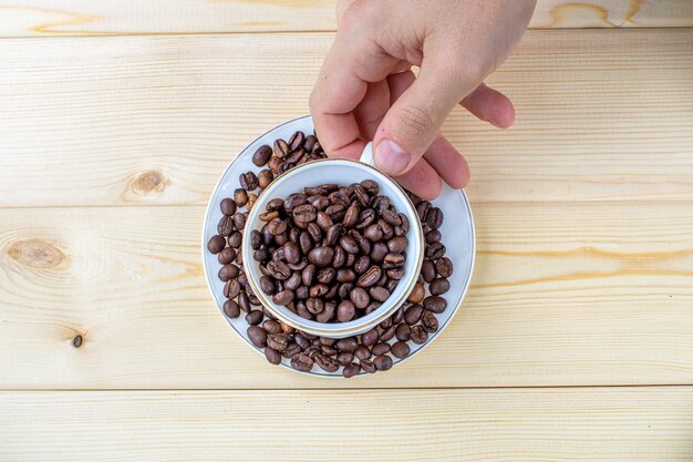 La mano di un uomo tiene una tazza bianca con chicchi di caffè su uno sfondo di legno.