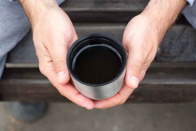 La mano di un uomo tiene una tazza di tè o caffè da un thermos.