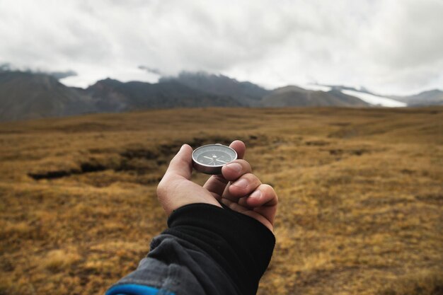 La mano di un viaggiatore tiene una bussola magnetica sullo sfondo di un paesaggio montuoso
