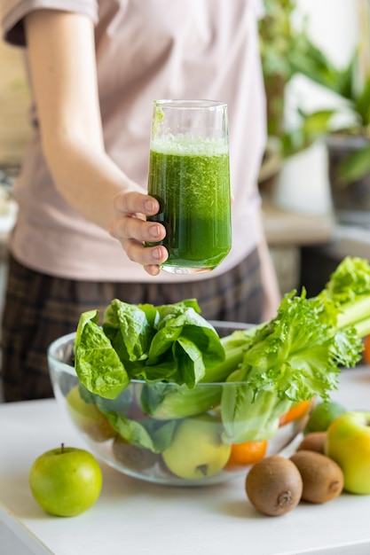 La mano di una donna bianca nella sua cucina prepara un frullato verde di frutta e verdura fresca
