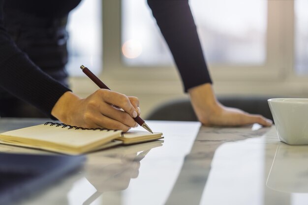 La mano di una donna che scrive in un blocco note catturata da vicino con uno sfondo vago