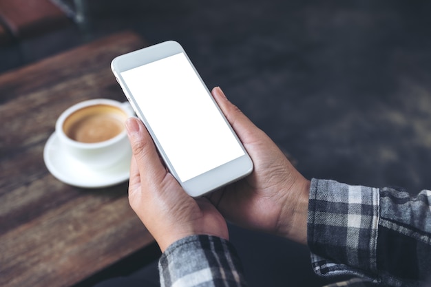 la mano di una donna che tiene il telefono cellulare bianco con schermo desktop vuoto con tazza di caffè