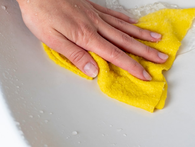 La mano di una donna con un panno giallo lava il lavandino. Il concetto di pulizia della casa