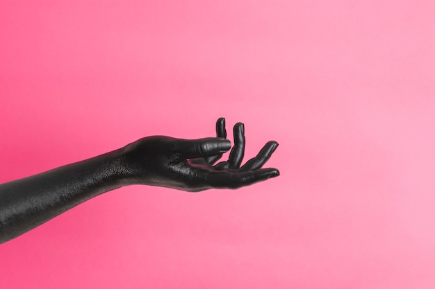 La mano di una donna elegante dipinta di nero sulla sua pelle gesticola su uno sfondo rosa concetto d'arte dell'alta moda