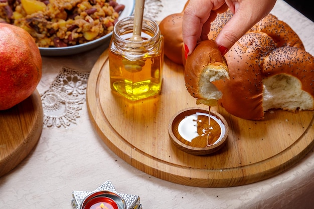 La mano di una donna immerge un pezzo di challah nel miele in onore della celebrazione di Rosh Hashanah vicino al miele e al challah e al cibo tradizionale
