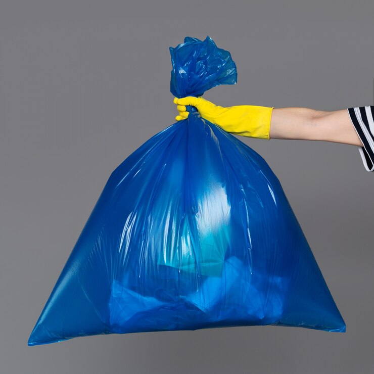 La mano di una donna in un guanto di gomma tiene un sacchetto di plastica blu pieno di immondizia.