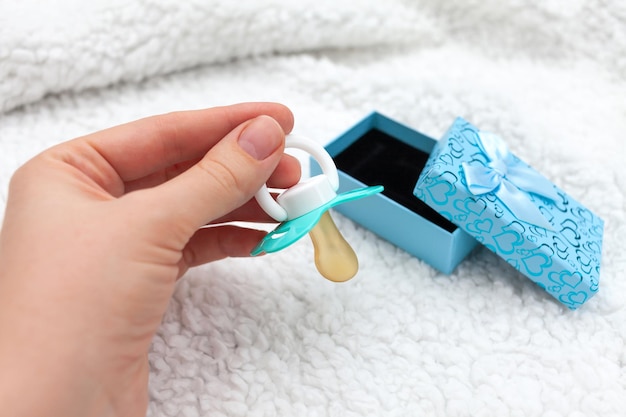 La mano di una donna prende un ciuccio blu da una confezione regalo