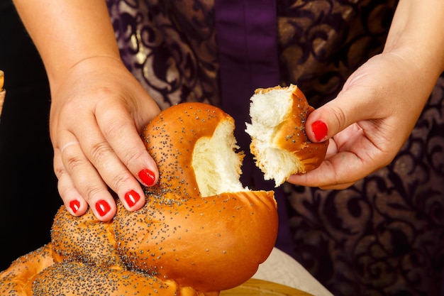 La mano di una donna rompe un challah su una tavola di legno durante le vacanze di Shabbat o Rosh Hashanah